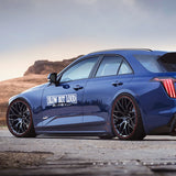 Blue car with 'Slow But Loud' decal on a road with mountains in the background