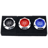 Three metallic oil filler caps in black, red, and blue on a black stand with a white background.