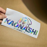 Holographic 'KAONASHI CLIQUE' sticker held over a brown surface