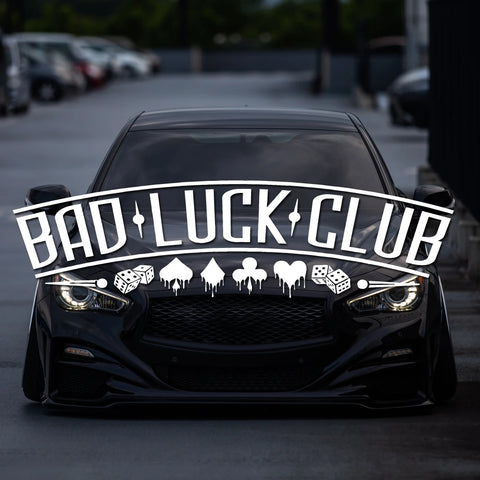 Black car with 'Bad Luck Club' decal in a parking lot