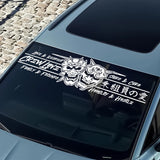 Car window with a decal featuring two masks and text on a stone pavement background