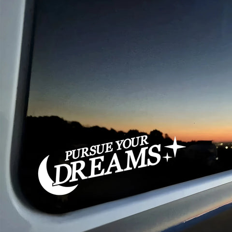 Window with 'Pursue Your Dreams' decal and sunset view