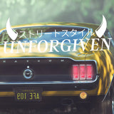Back view of a yellow car with 'UNFORGIVEN' text and logo on a blurred green background