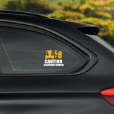 Car sticker with 'Caution: Electric Shock' text on a black car window with a blurred green background.
