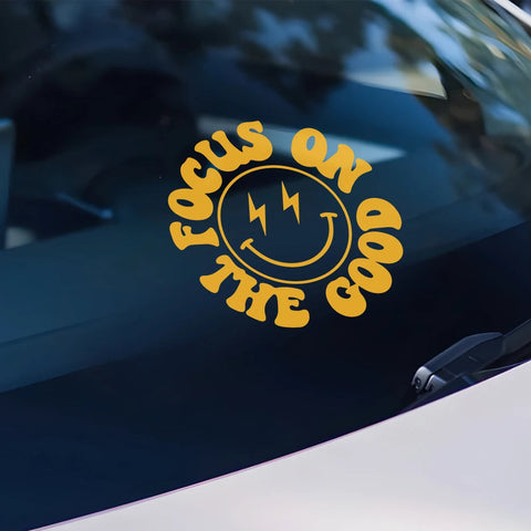 Yellow 'Focus on the Goal' smiley face sticker on a car window with text about Roland equipment.