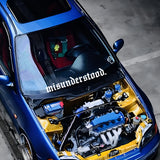 Car with open hood showing engine and 'misunderstood' decal on windshield.