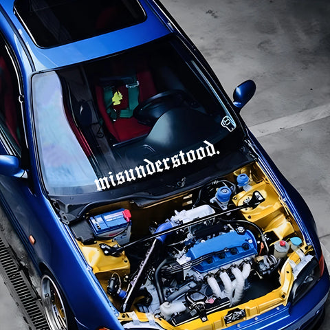 Car with open hood showing engine and 'misunderstood' decal on windshield.