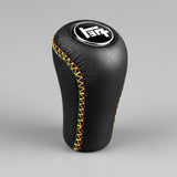 Black gear shift knob with colorful stitching on a dark background