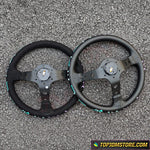 Two black steering wheels on a textured gray surface with 'TopJDMStore.com' logo.