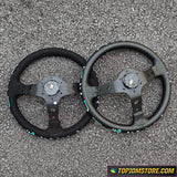 Two black steering wheels on a textured gray surface with 'TopJDMStore.com' logo.