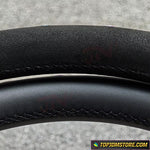 Close-up of a black leather steering wheel with visible stitching on a gray background.