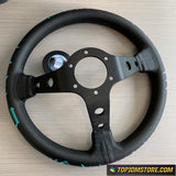 Black steering wheel with a central hub on a light wood surface, featuring the TopJDMStore.com logo.