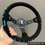 Black steering wheel with decorative patterns held by a hand against a gray background