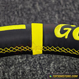 Close-up of a black steering wheel cover with yellow stitching and 'G' logo on a textured gray background.